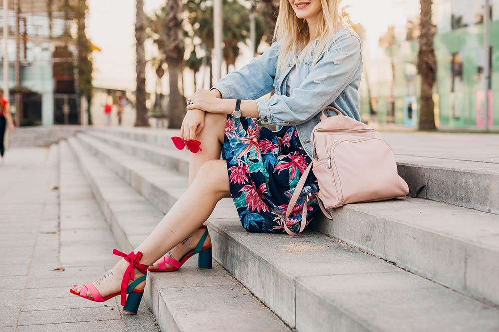 γυναικεία ανοιξιάτικα παπούτσια με χρώμα και τακούνι και τα φοράει μία κοπέλα καθισμένη σε σκαλάκια και χαμογελάει