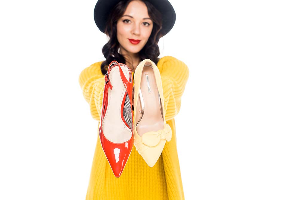 κόκκινο και κίτρινο ανοιξιάτικο παπούτσι το κρατάει μία κοπέλα και χαμογελάει