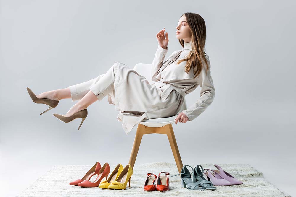κοπέλα καθισμένη σε καρέκλα με τα πόδια στον αέρα και 6 ζευγάρια γυναικεία ανοιξιάτικα παπούτσια σε διάφορα χρώματα